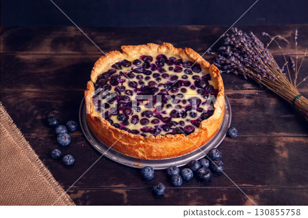 Rustic shortbread pie with blueberries in sour cream filling on a wooden background and a bouquet of dried lavender. Rustic shortbread pie with blueberries in sour cream filling on a wooden background and a bouquet of dried lavender. 130855758