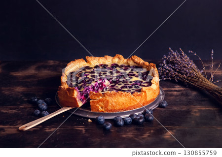 Rustic shortbread pie with blueberries in sour cream filling on a wooden background and a bouquet of dried lavender. Rustic shortbread pie with blueberries in sour cream filling on a wooden background and a bouquet of dried lavender. 130855759