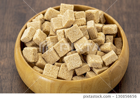 Organic brown sugar cubes in wooden bowl rustic style natural sweetener healthy ingredient close up textured surface kitchen table cozy atmosphere Organic brown sugar cubes in wooden bowl rustic style natural sweetener healthy ingredient close up textured surface kitchen table cozy atmosphere 130856656