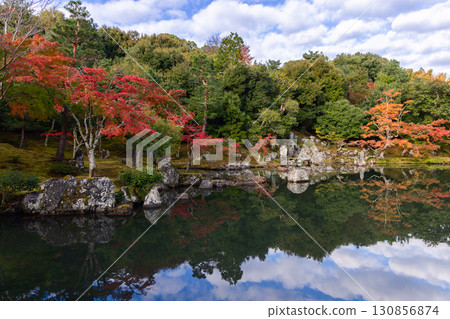 Japanese park with fiery autumn foliage and stones reflecting in water under warm evening glow Japanese park with fiery autumn foliage and stones reflecting in water under warm evening glow 130856874