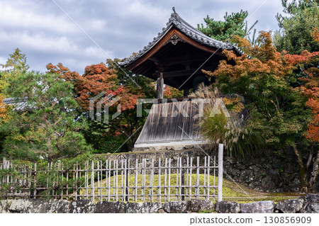 Wooden belfry in Tenryu ji Kyoto framed by red maple leaves and bamboo fence in serene autumn scene 130856909