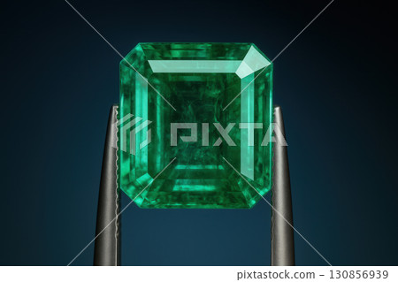 Emerald Gemstone in Tweezers against Deep Blue Background 130856939