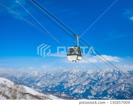 A ski resort gondola lift moving above snowy mountains and a spectacular winter view (Nagano Prefecture, Hakuba, Tsugaike Highlands) 130857009