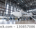 White passenger plane in the airplane hangar. Aircraft under maintenance. Checking mechanical systems for flight operations 130857086