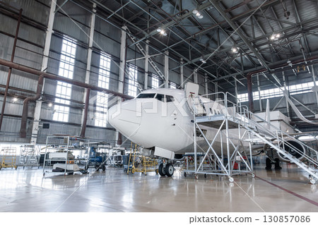 White passenger plane in the airplane hangar. Aircraft under maintenance. Checking mechanical systems for flight operations 130857086