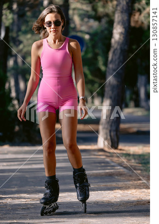 Woman in pink sportswear rollerblading in the park on a sunny day, active fitness concept. Woman in pink sportswear rollerblading in the park on a sunny day, active fitness concept. 130857141