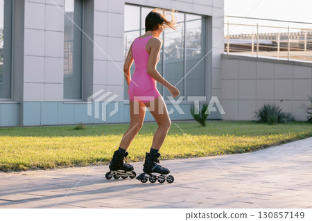 Sexy woman in pink sportswear rollerblading outdoors on a sunny day, active lifestyle and fitness concept. 130857149
