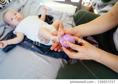 Close up Father massages baby's legs with massage ball. Healthy massage. Massage therapist. Sensory tactile activities. Massage textured balls for kids. Earlier development. Focus picked. 130857257