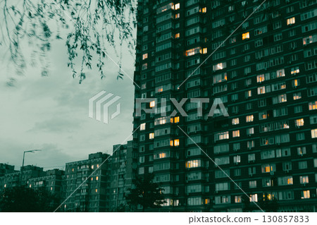 An evening shot of apartment buildings with lit windows, framed by tree branches, creating a peaceful atmosphere. dusky sky, perfect for ambiance. 130857833