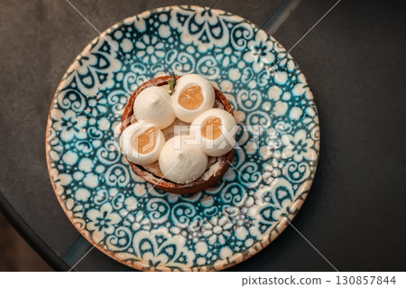 A top-down shot of a pastry tart served on a patterned blue plate, showcasing intricate design. The elegant dessert has white cream and fruit filling. 130857844