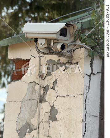 Security camera mounted on cracked building wall showing urban decay and infrastructure 130857911