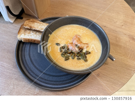 Pumpkin soup with shrimp and pumpkin seeds on a plate with toast, served on a wooden table Pumpkin soup with shrimp and pumpkin seeds on a plate with toast, served on a wooden table 130857916