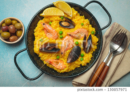 Spanish seafood Paella with shrimps, mussels, peas and lemon in a pan on light blue background top view. Mediterranean meal 130857971
