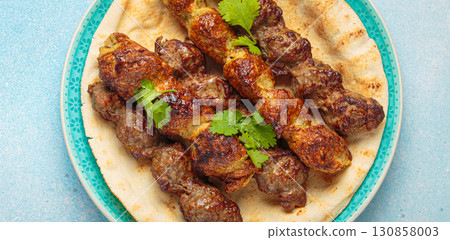 Kofta meat kebabs with pita bread, tomato sauce, and coriander on blue plate top view on light beige background 130858003