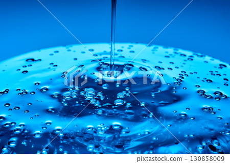 The viscous gel serum for the face flows and collects into a drop on a blue background.. 130858009