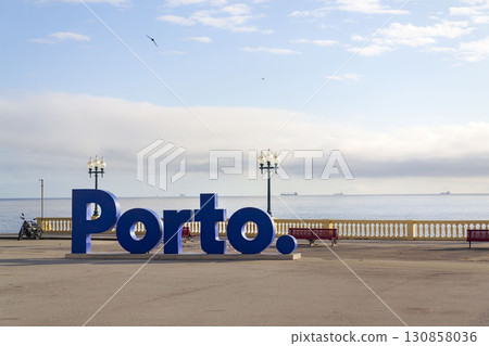 Blue three-dimensional Porto sign on promenade along the coast and beach, Portugal, sunset on sunny summer day 130858036