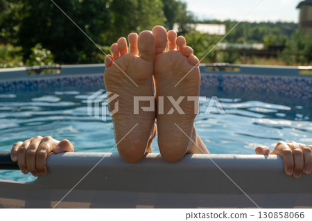 Relaxing summer day by the pool with person lounging and feet in focus 130858066