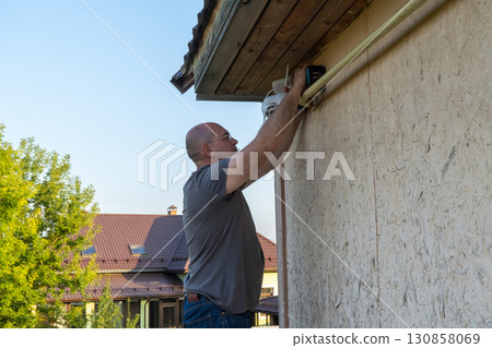 Caucasian adult male installing security camera outdoor on wall Caucasian adult male installing security camera outdoor on wall 130858069