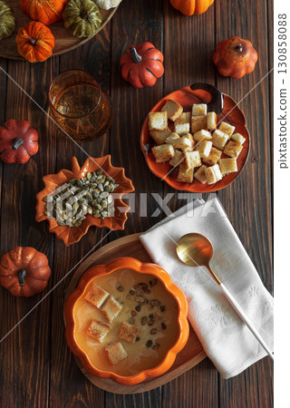 Creamy pumpkin soup with croutons and seeds, served in a pumpkin-shaped bowl on dark wooden table. Top view Creamy pumpkin soup with croutons and seeds, served in a pumpkin-shaped bowl on dark wooden table. Top view 130858088
