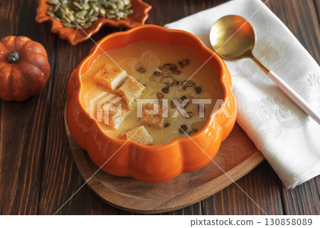 Creamy pumpkin soup with croutons and seeds, served in a pumpkin-shaped bowl on dark wooden table. Top view Creamy pumpkin soup with croutons and seeds, served in a pumpkin-shaped bowl on dark wooden table. Top view 130858089