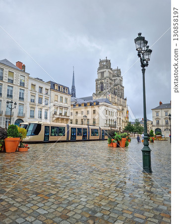 Orleans city center and a tram moving across the wet cobblestone square, with the ornate towers of the Sainte-Croix cathedral visible in background Orleans city center and a tram moving across the wet cobblestone square, with the ornate towers of the Sainte-Croix cathedral visible in background 130858197