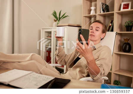 Relaxing professional with coffee checking phone at desk in home office 130859337