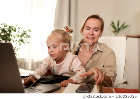 Mother and daughter interacting with a laptop in a home office 130859356