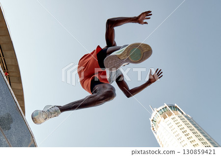 Low angle view of athlete jumping amidst urban skyscrapers on a bright day 130859421