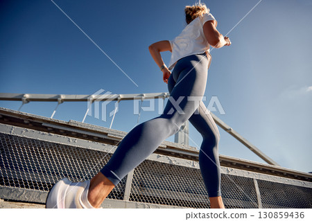 Woman jogging on a bridge under bright blue sky in urban environment 130859436