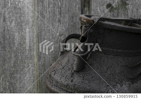 Black and oiled metal canister in the countryside. Wooden wall in background 130859915