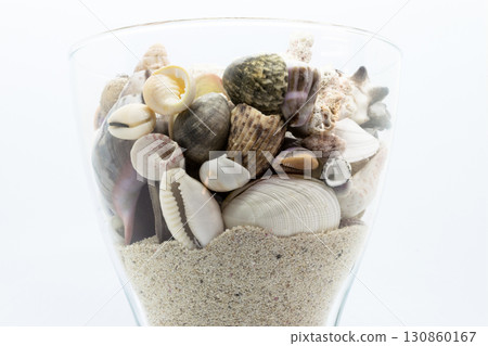Glass Filled with Seashells, Corals and Beach Sand in White Background Glass Filled with Seashells, Corals and Beach Sand in White Background 130860167