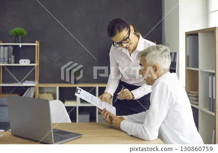 Senior businessman reads a document brought to him by his secretary before signing it. 130860759