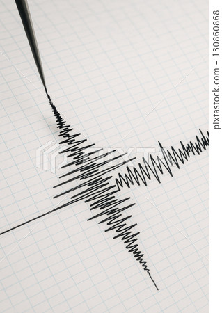 Seismograph recording earthquake waves on graph paper showing natural disaster data and geology research concept with black ink lines and grid background 130860868