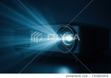Modern digital projector emitting bright blue light rays in dark room, showcasing cinematic technology with futuristic illumination and sleek design for home theater or presentations 130860908