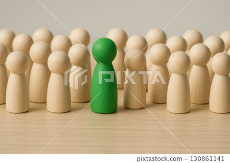 Green figurine standing among crowd of beige wooden figures symbolizing leadership and individuality concept with minimal composition and soft lighting Green figurine standing among crowd of beige wooden figures symbolizing leadership and individuality concept with minimal composition and soft lighting 130861141