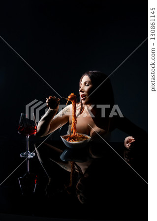 Woman enjoying spaghetti in a studio while seated at a dark table 130861145