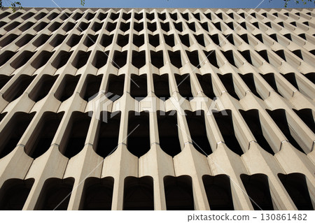 The facade of a modernist building features a repeating pattern of concrete forms. The design creates an interesting interplay of light and shadow. 130861482