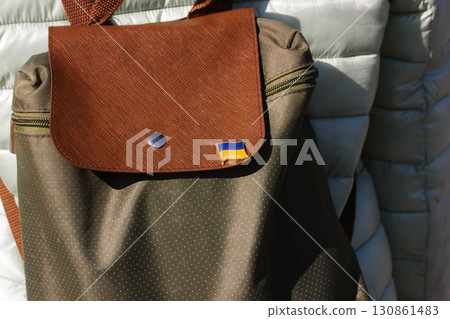A brown and green backpack with the flag of Ukraine pinned on it, showing support. A shot is taken during a day, with good lighting Ukrainian flag pin 130861483