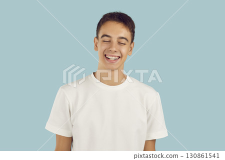 Smiling young boy wearing casual white t-shirt standing with closed eyes on blue background Smiling young boy wearing casual white t-shirt standing with closed eyes on blue background 130861541