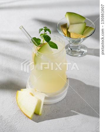 Cold lemonade or mojito in a glass with melon, straw and mint on a light background Cold lemonade or mojito in a glass with melon, straw and mint on a light background 130861607