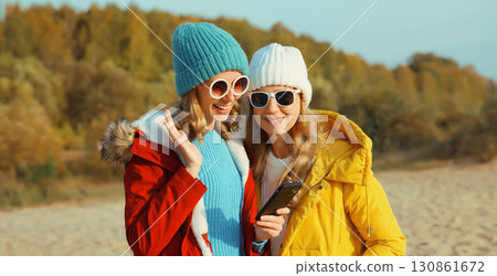 Happy young women friends with smartphone together on beach, smiling girlfriends using phone on sea Happy young women friends with smartphone together on beach, smiling girlfriends using phone on sea 130861672