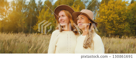 Happy two women friends looking away in autumn park, stylish smiling girlfriends standing outdoors 130861691