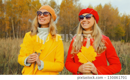 Happy young two women friends with autumn yellow leaves, stylish girlfriends smiles together in park 130861701