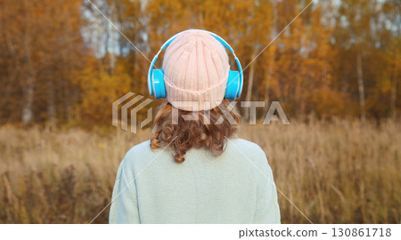 Inspired young woman enjoying listening to music in headphones outdoors in autumn forest 130861718