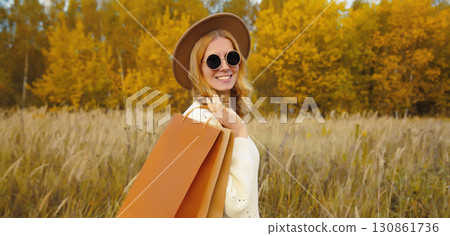 Stylish happy woman standing with shopping bag in autumn park, fashionable girl smiling outdoors Stylish happy woman standing with shopping bag in autumn park, fashionable girl smiling outdoors 130861736