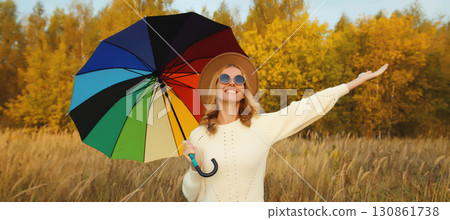 Happy young woman with colorful umbrella in autumn park, enjoys warm weather, fall season background Happy young woman with colorful umbrella in autumn park, enjoys warm weather, fall season background 130861738