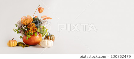 Creative autumn floral arrangement of seasonal flowers in pumpkin as vase on gray background for Thanksgiving Day. Annual decorations. Copy space. Banner. 130862479