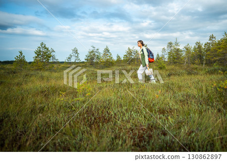 Joyful active woman forager walking after mushroom picking on raised peat bog in forest wetlands Joyful active woman forager walking after mushroom picking on raised peat bog in forest wetlands 130862897