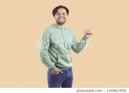 Smiling happy bearded guy is pointing index finger on copy space on beige background. Smiling happy bearded guy is pointing index finger on copy space on beige background. 130862940
