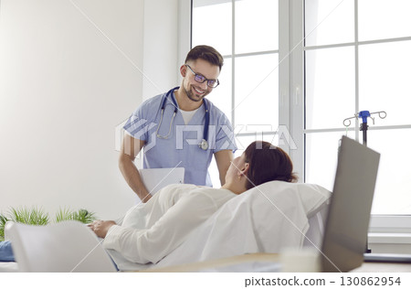 Friendly male nurse gives IV line to woman patient who is lying on medical bed at clinic 130862954